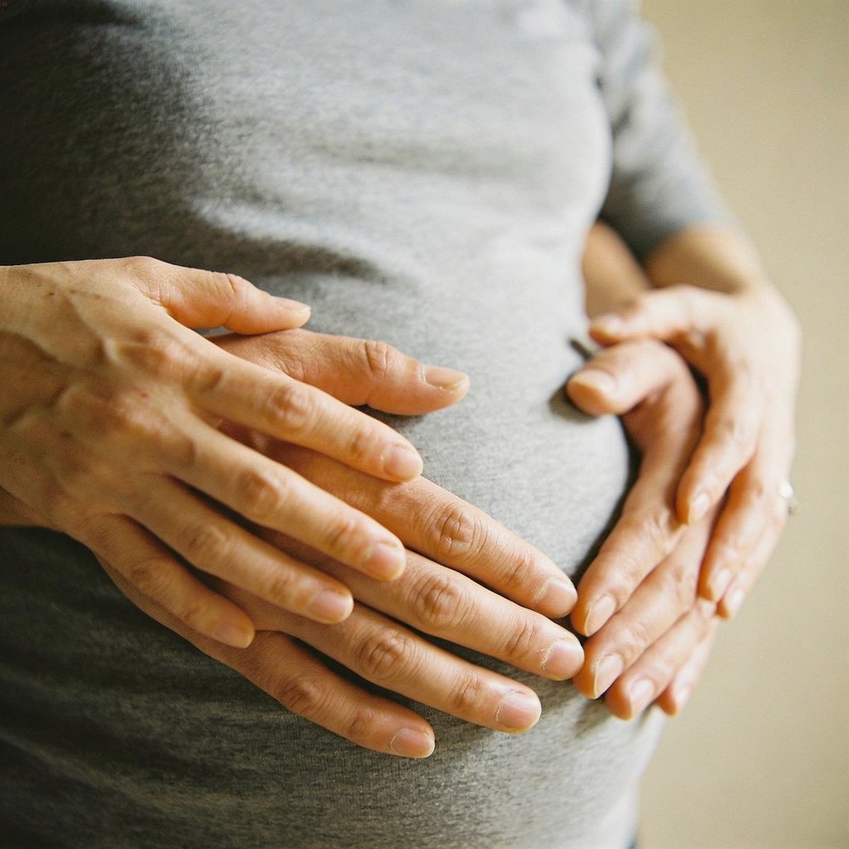 Gros plan des mains de la future maman et du papa formant un cœur sur le ventre rond